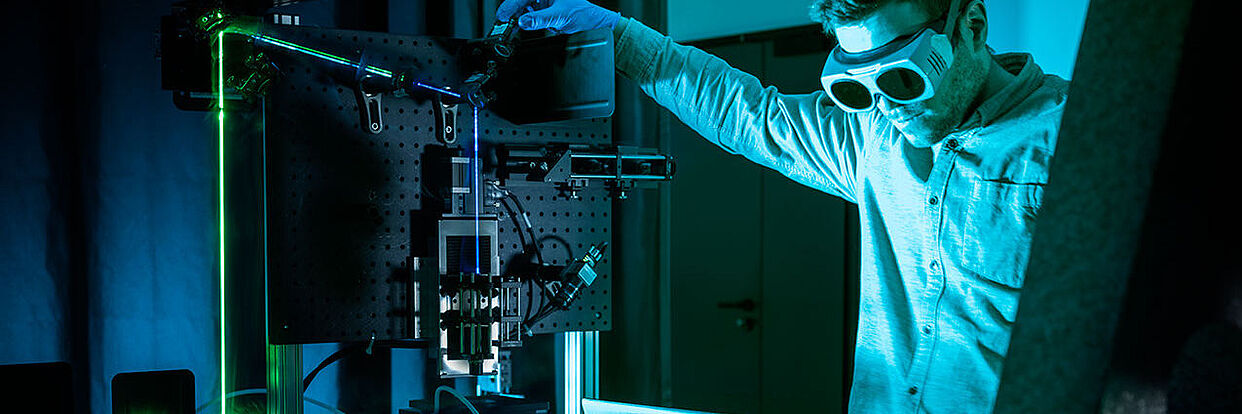 Ein Mensch im Labor-Overall arbeitet an einer Laserapparatur.